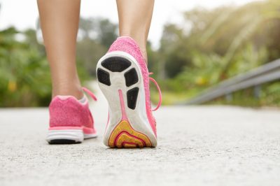 Cropped rear shot of athletic girl wearing pink sneakers while hiking or jogging on pavement outdoors. Woman jogger with fit beautiful legs doing workout. Selective focus, freeze action shot